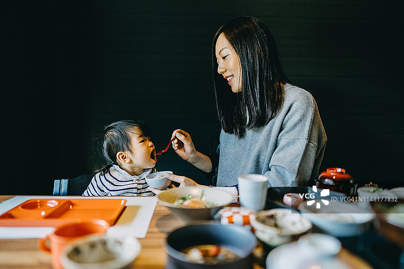 年轻的妈妈一边照顾可爱的小女儿，一边享受精致的日本料理图片素材