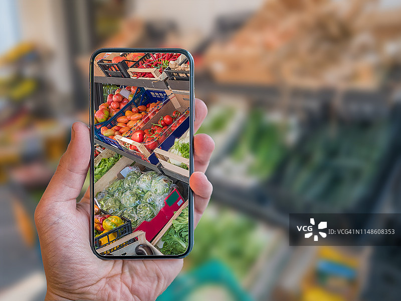 增强现实购物手机应用。手拿手机与AR应用扫描蔬菜在食品市场。图片素材