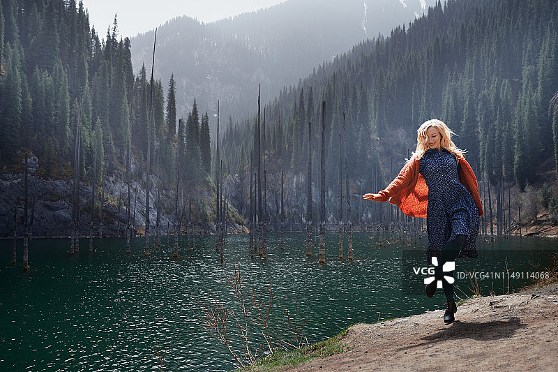 快乐的女人在山上的湖泊和淹没的树木图片素材