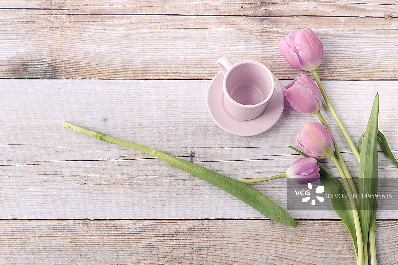 粉红色的郁金香花和空的粉红色咖啡杯在木制背景上。直接在上面复制空间。图片素材