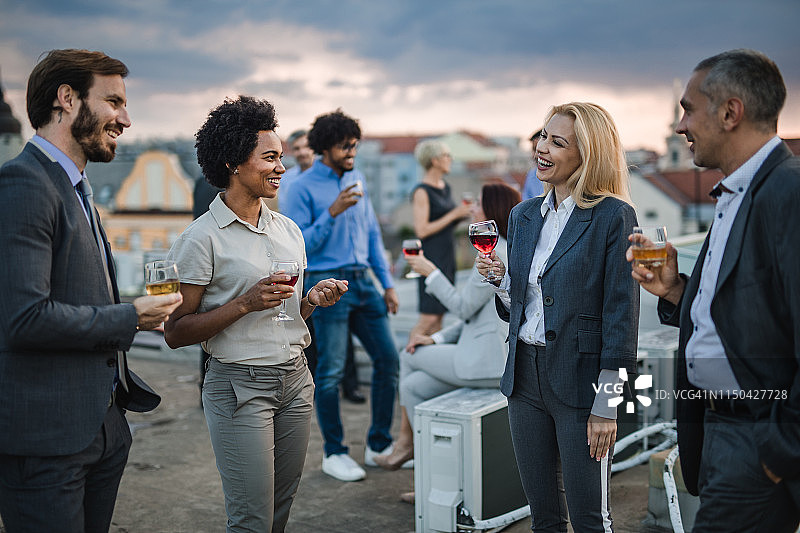 在屋顶派对上，快乐的商业人士一边喝酒一边聊天。图片素材