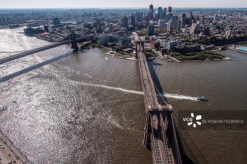 从布鲁克林上空俯瞰曼哈顿一侧的直升机上拍摄的横跨东河的布鲁克林桥和曼哈顿桥。一些船正从桥下经过图片素材