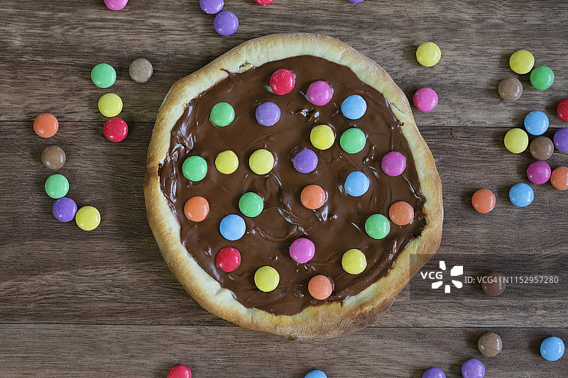 图片自制的巧克力披萨与多色糖果糖果和糖霜糖，烤披萨皮充满榛子巧克力涂抹儿童，顶部是脆糖涂层彩虹smarties巧克力糖果，吃布丁甜点图片素材