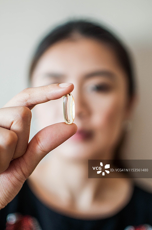 一名年轻的亚洲妇女拿着一粒药物凝胶胶囊，背景是白色的图片素材