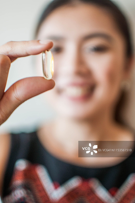 一名年轻的亚洲妇女拿着一粒药物凝胶胶囊，背景是白色的图片素材