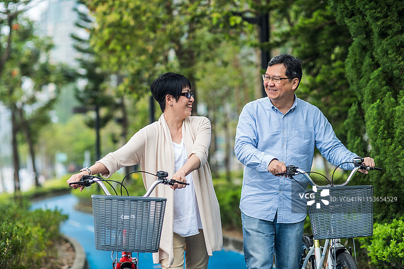 年老的亚洲夫妇骑着自行车在公园里。图片素材