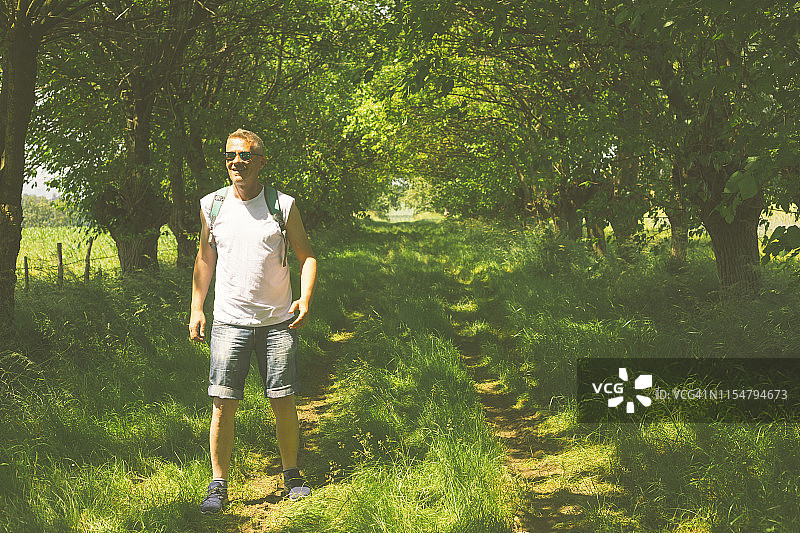 快乐微笑的成人徒步者戴着太阳镜在美丽阳光明媚的夏日徒步大自然图片素材