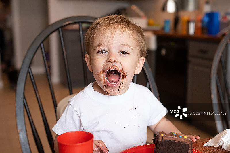 在他的生日派对上，3岁的金发男孩脸上满是巧克力蛋糕，笑得很开心图片素材
