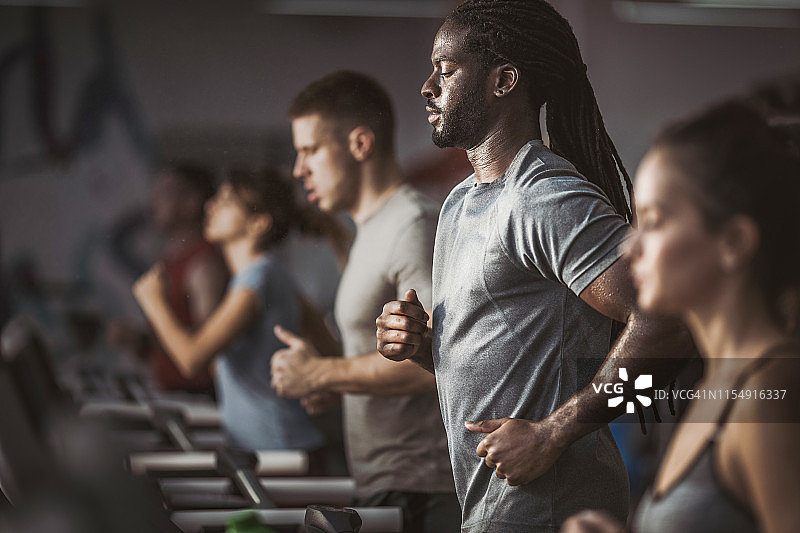 非裔美国运动员，在健身房跑步机上和其他运动员一起跑步。图片素材