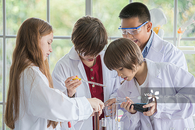 一群穿着白袍的学生在学校的实验室里做化学实验。在科学实验室里，孩子们用吸管将液体滴到试管中进行研究。多民族。亚洲人,白人,生物化学图片素材