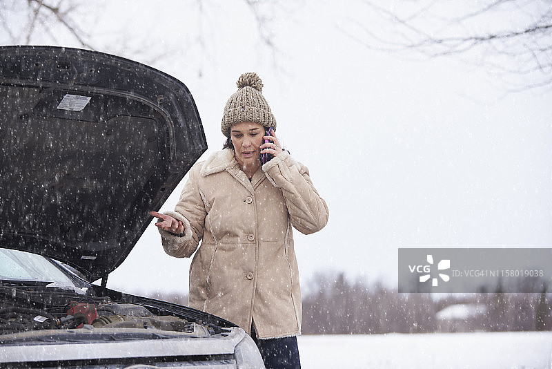 一个女人在抛锚的车旁边用手机。图片素材