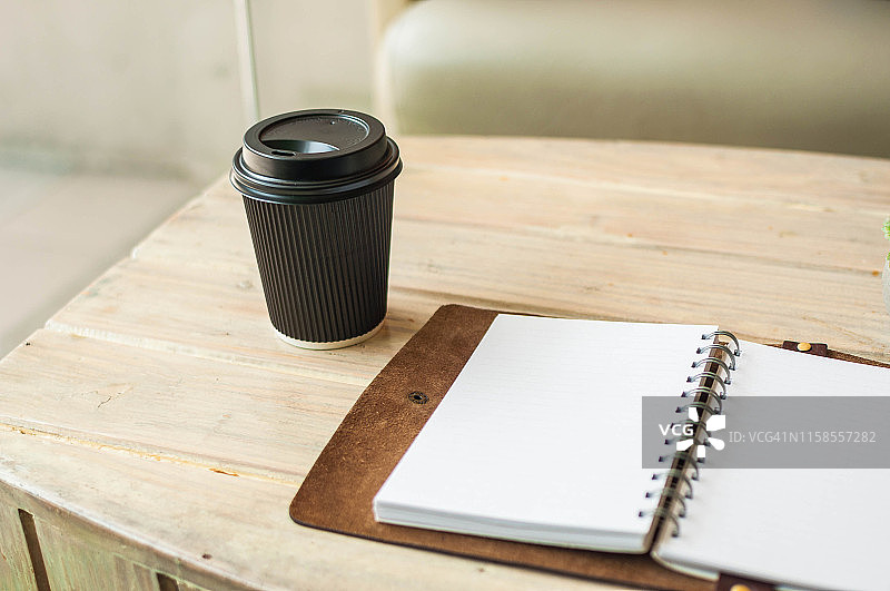一个私人记事本，黑色的纸和塑料咖啡杯放在一个木桌上的静物画图片素材