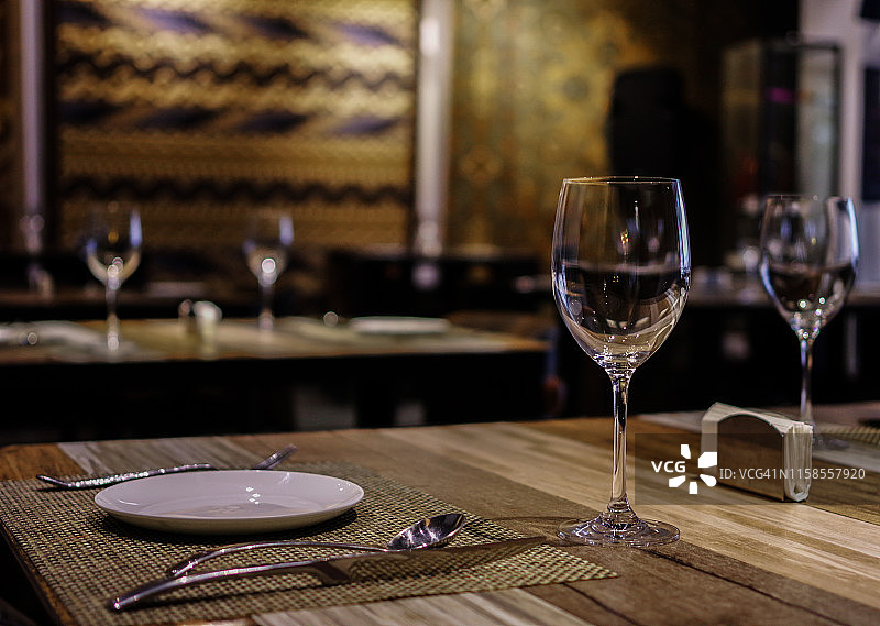 空酒杯和白色盘子，刀叉在餐厅的木桌上，墙上挂着丝绸地毯图片素材