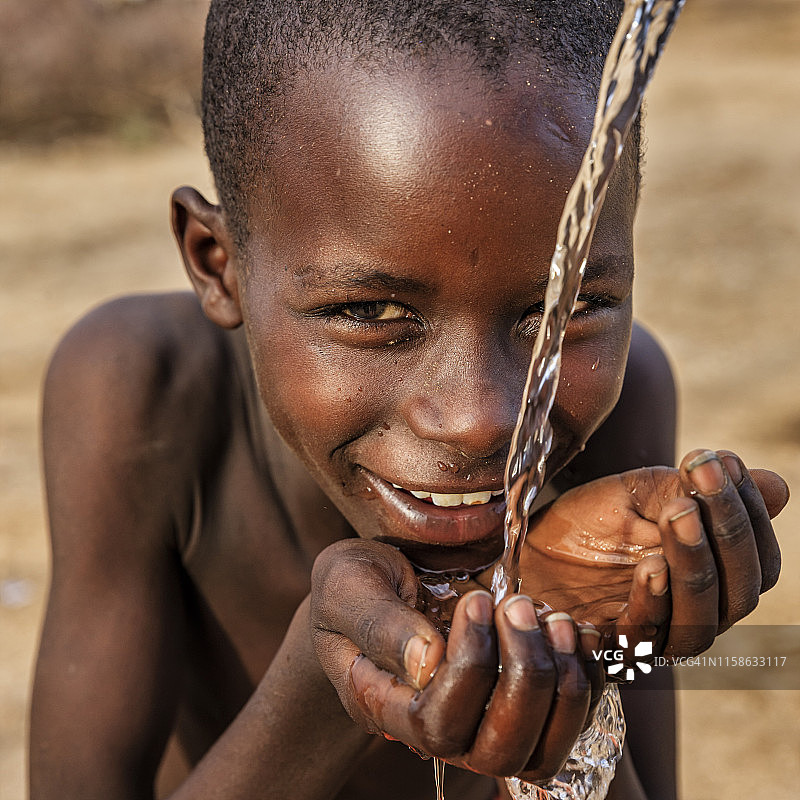 非洲小男孩在非洲东部的稀树草原上喝着淡水图片素材