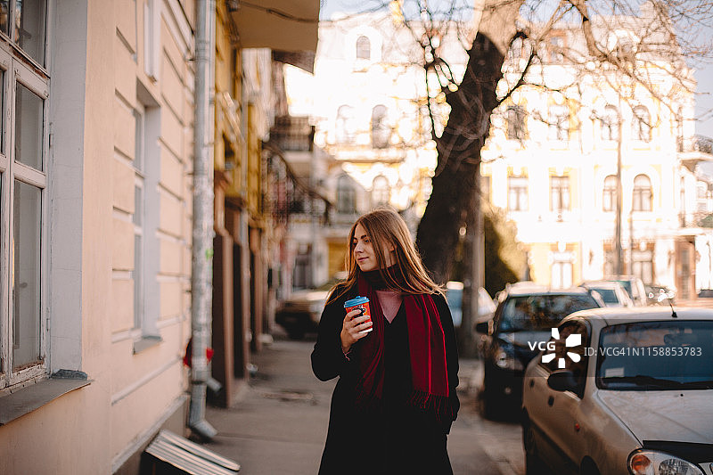 年轻女子拿着咖啡杯走在人行道上的肖像图片素材