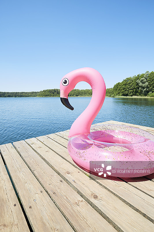 粉红色的充气火烈鸟在一个码头上，在田园诗般的湖对着蓝色的天空图片素材