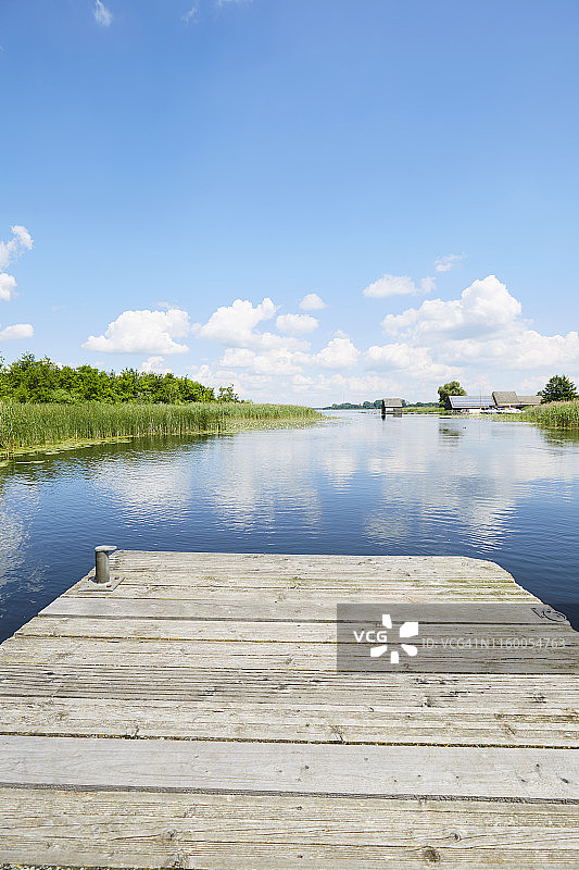 在田园诗般的湖边，芦苇草映衬着蓝天，云朵倒映在水中图片素材