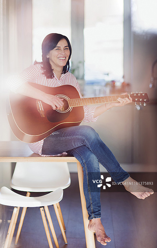 微笑的成熟女人在家里弹吉他图片素材