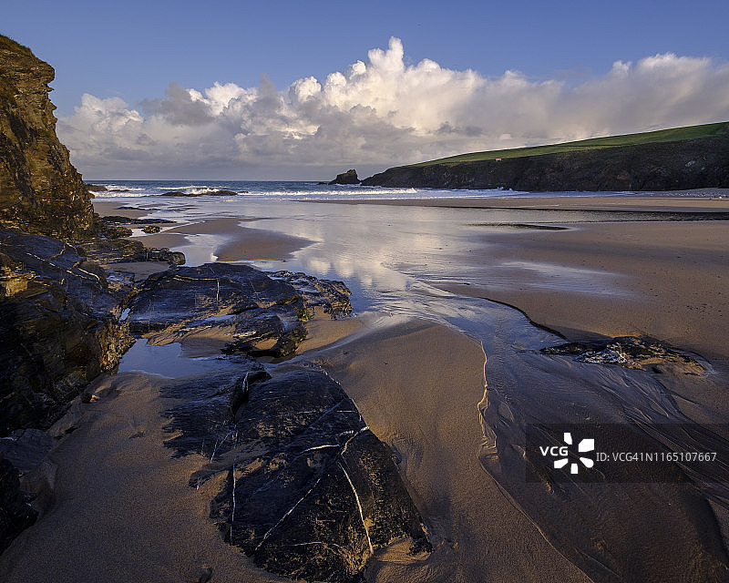 大西洋的云层将黎明的阳光反射到特里沃尼潮湿的沙滩和岩石上，靠近帕德斯托，英国，欧洲图片素材