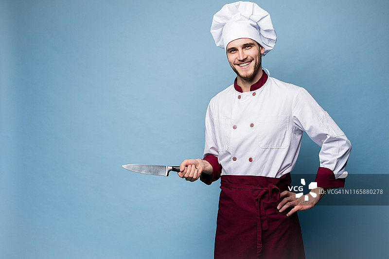 一个英俊的男厨师的肖像厨师拿着刀孤立在浅蓝色的背景。图片素材