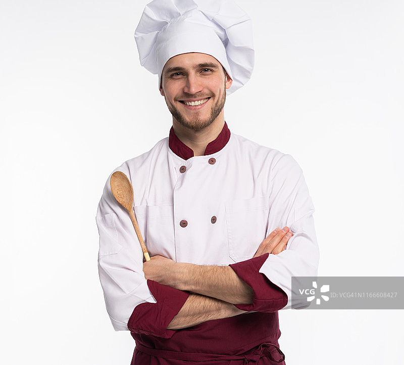 正面牙齿厨师厨师在贝雷帽的肖像，白色服装有工具在交叉的胳膊看在白色背景孤立的相机。图片素材