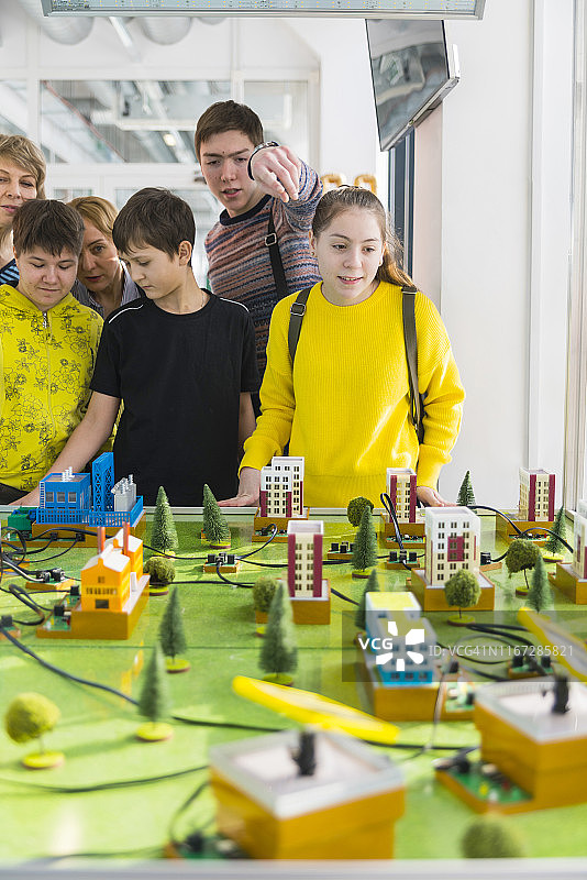这个十几岁的男孩在科学技术大厅里用一个巨大的城市模型向一群孩子和成年人解释电力是如何工作的图片素材