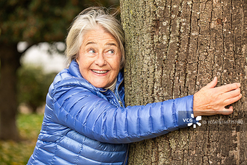 一个漂亮的老女人抱着一棵树的肖像。图片素材