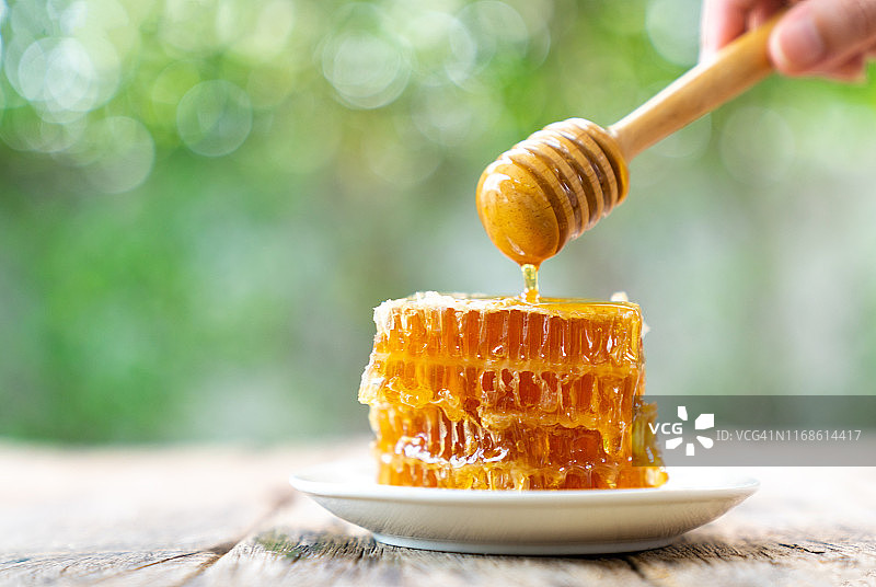 蜂蜜滴从一个木制的蜂蜜勺在木制的灰色乡村背景上的一个罐子，蜂蜜，蜂巢，蜂蜜蜜蜂。图片素材