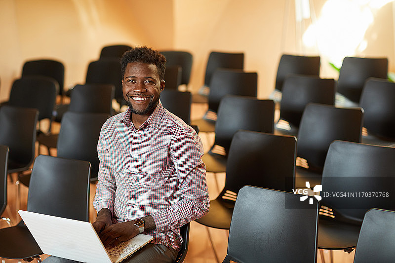 照片中，年轻英俊的黑人经理穿着衬衫坐在会议室的椅子上，使用笔记本电脑图片素材