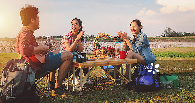 一群亚洲朋友玩尤克里里和花时间在夏季假期野餐。他们在假期很快乐，玩得很开心。图片素材