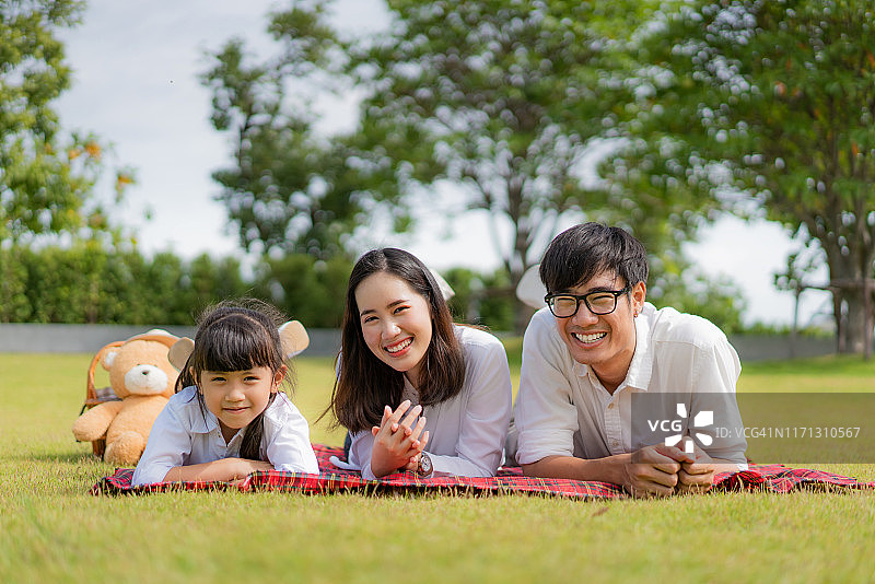 美丽幸福的亚洲家庭享受时刻躺在绿色的草地上在公园看在镜头。图片素材