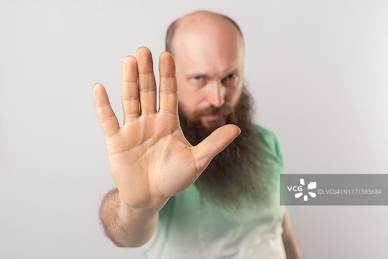 阻止它。严肃的中年秃顶男人的肖像在淡绿色t恤站与停止手势和看着相机。图片素材