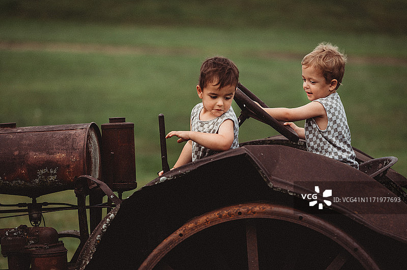 3岁的异卵双胞胎坐在爱荷华州农场的一辆生锈/古董/古董拖拉机上图片素材