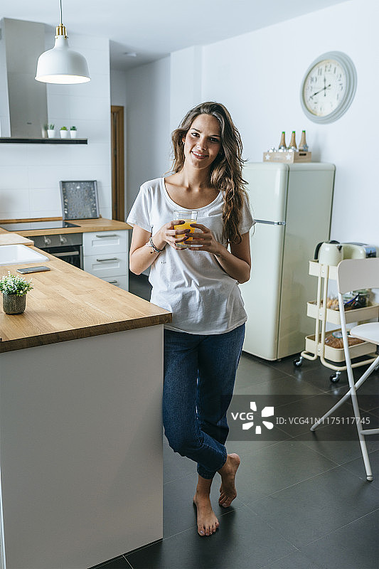 微笑的年轻女子在厨房喝橙汁的肖像图片素材