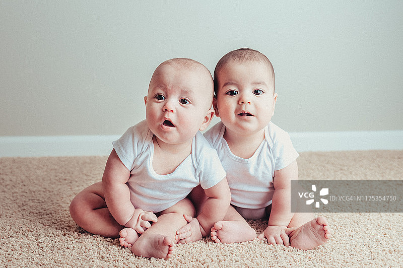 7个月大的雄性异卵双胞胎穿着白色连体衣坐在地毯上图片素材