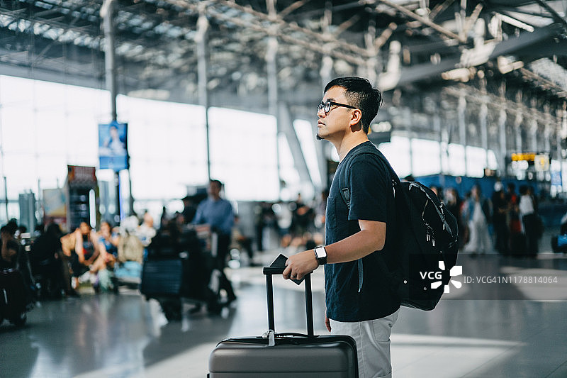 年轻的亚洲男性背包客拿着护照和行李箱走在国际机场大厅里图片素材