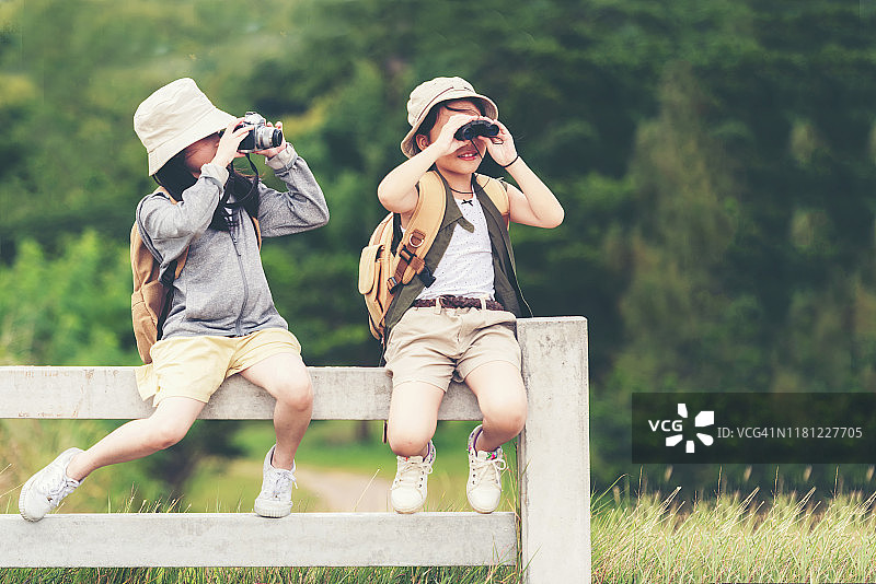 亚洲两名儿童游客拍照和看望远镜，人们女孩坐在白色的围栏户外探险，旅游目的地休闲旅游在自然公园。旅游度假的概念图片素材