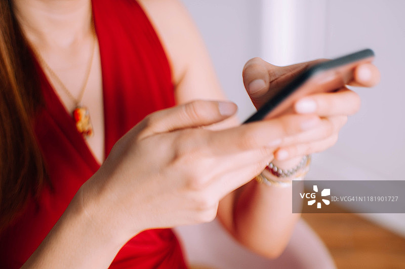 一位身穿红色连衣裙的年轻女子正在室内使用手机图片素材