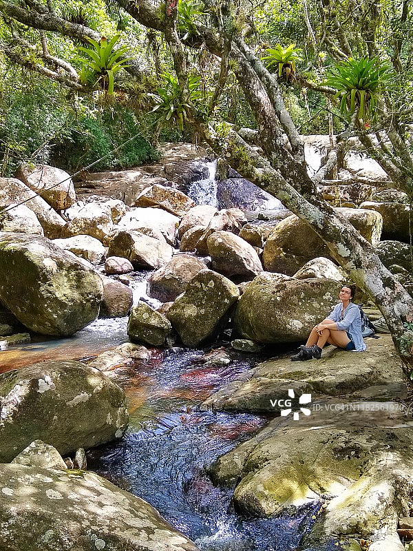 在巴西圣卡塔琳娜，Florianópolis的大西洋森林里，女孩在一条河里的岩石里图片素材