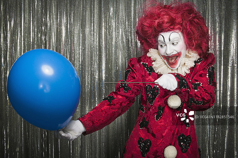 一个小丑准备用针扎破气球图片素材