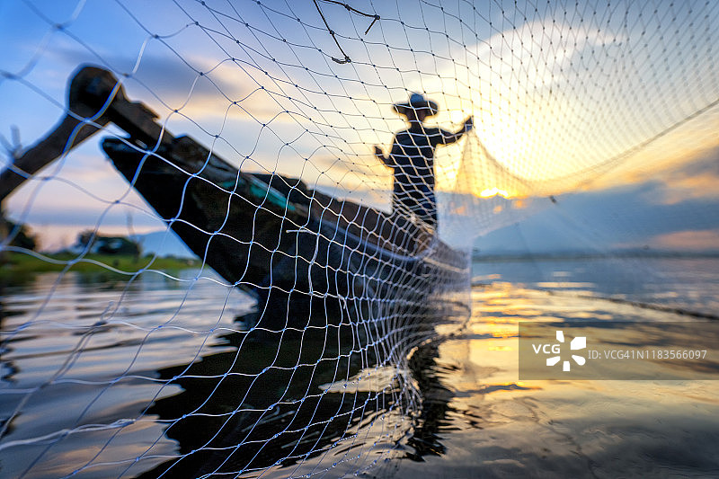 亚洲渔民在木船上的剪影，在大自然的河流在清晨撒网捕捉淡水鱼。图片素材