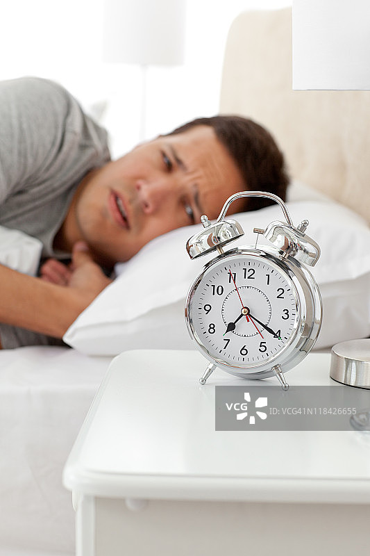 一个不快乐的人躺在床上看他的闹钟图片素材