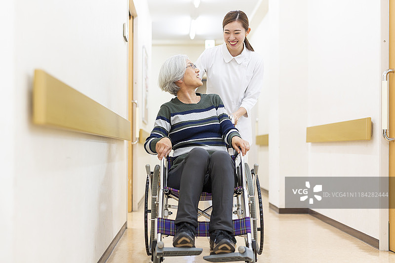 护士推着一位坐轮椅的老年病人穿过医院图片素材