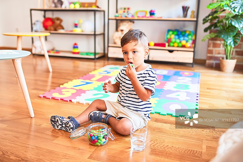 美丽的学步男孩坐在拼图上吃小彩色巧克力球在幼儿园图片素材