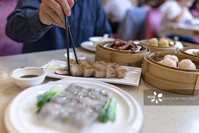 亚洲男子拿起点心与筷子，享受各种各样的中国点心在餐厅图片素材