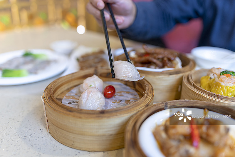 亚洲男子拿起点心与筷子，享受各种各样的中国点心在餐厅图片素材
