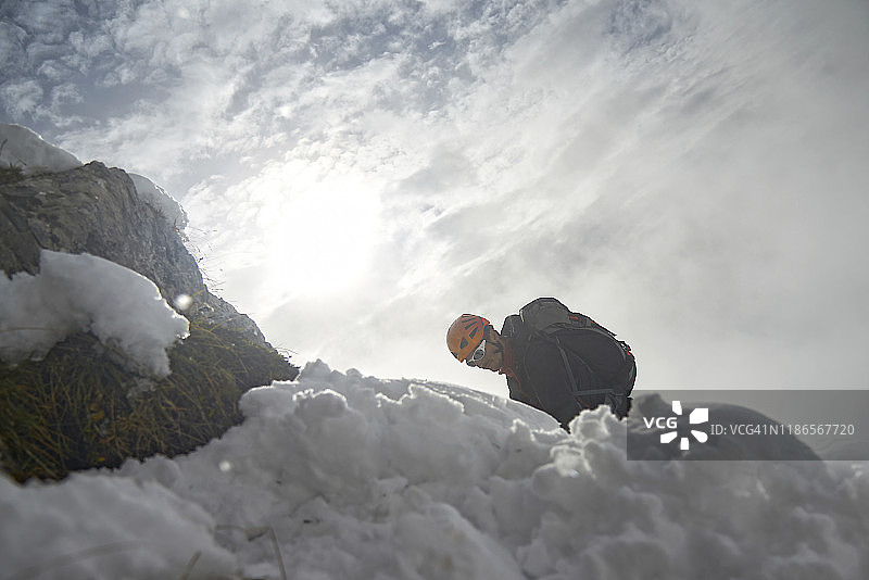 低角度的徒步旅行者在雪山上反对多云的天空在冬天图片素材