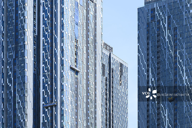 一些现代摩天大楼的特写镜头，一些窗户清洗机在一个悬挂的平台上工作，马来西亚吉隆坡。图片素材
