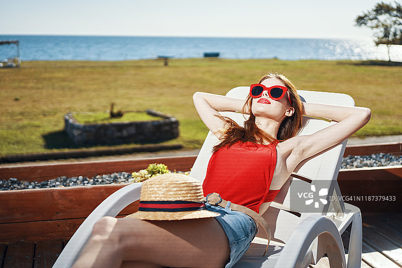 一个女人躺在日光浴床上，在泳池边晒太阳图片素材