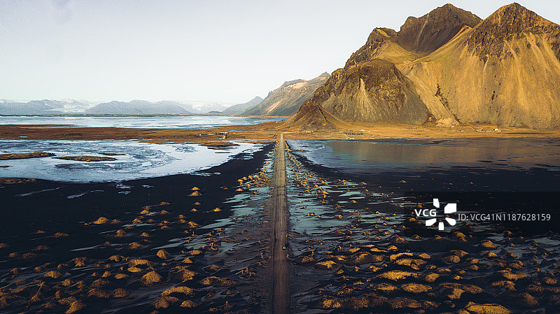 在冰岛东部，一辆汽车在沙丘、山脉和大海的戏剧性景观中行驶的鸟瞰图图片素材